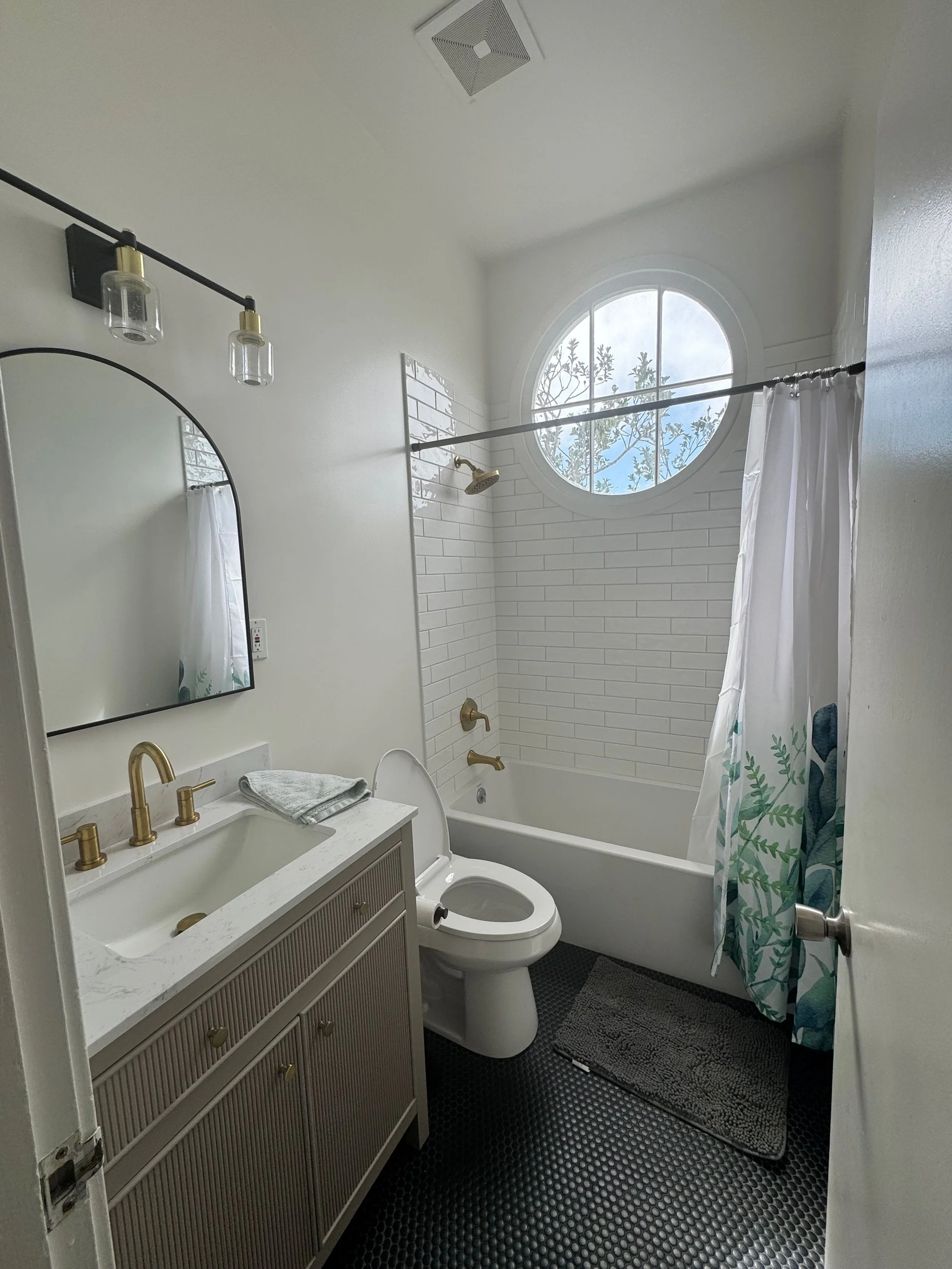 Bathroom after remodel — modern vanity with arched mirror, hex tile floor, round window